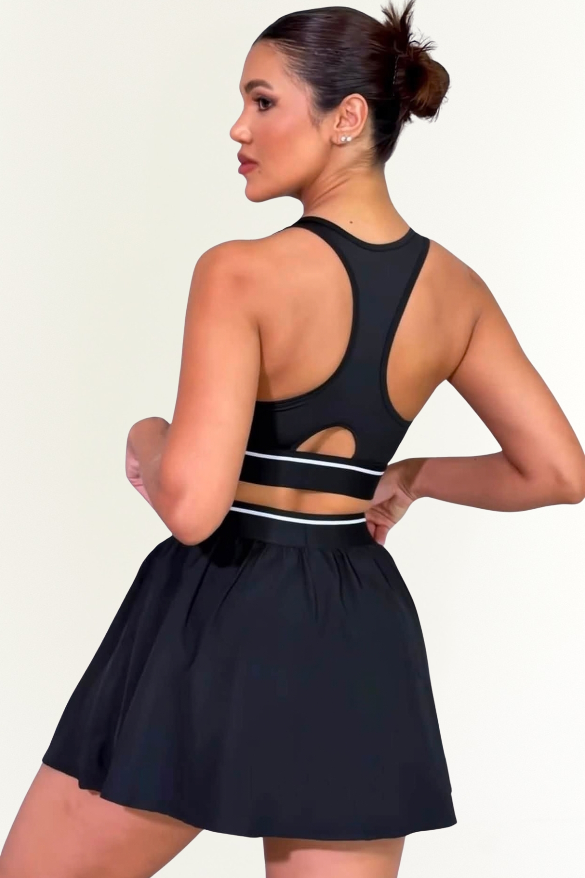 Conjunto deportivo negro de mujer con top de copa fija y pollera short perfil de espalda